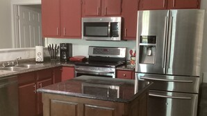 A modern kitchen with stainless steel appliances, a central island, and red cabinetry.