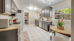 A modern kitchen with granite countertops, a built-in microwave, and a dining area with a wooden table and chairs. - Orange Grove (Melbourne)