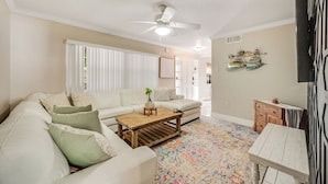 A living room with a white sofa, a wooden coffee table, a ceiling fan, and a colorful rug. - Orange Grove (Melbourne)
