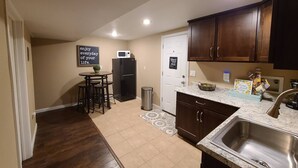 A compact kitchen with dark wooden cabinets, a stainless steel sink, a refrigerator, and a microwave. There is a small dining area with stools and a sign on the wall. - Entire guest suite in Colorado Springs, Colorado (Colorado Springs)