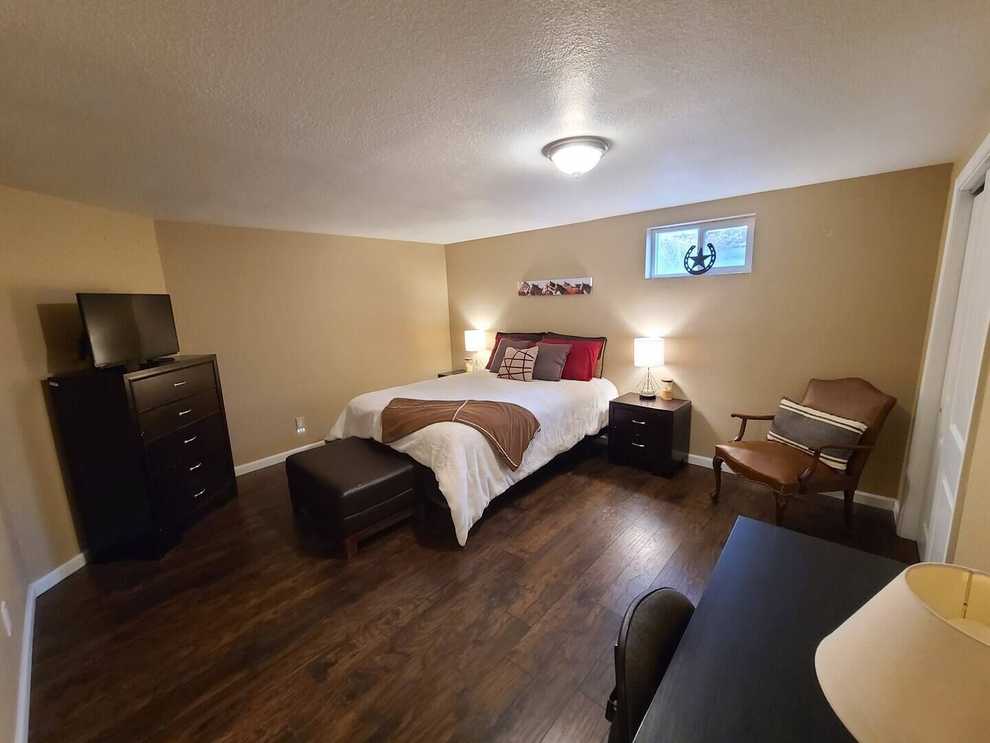 A bedroom with a bed, a desk, a chair, a dresser, and a television.