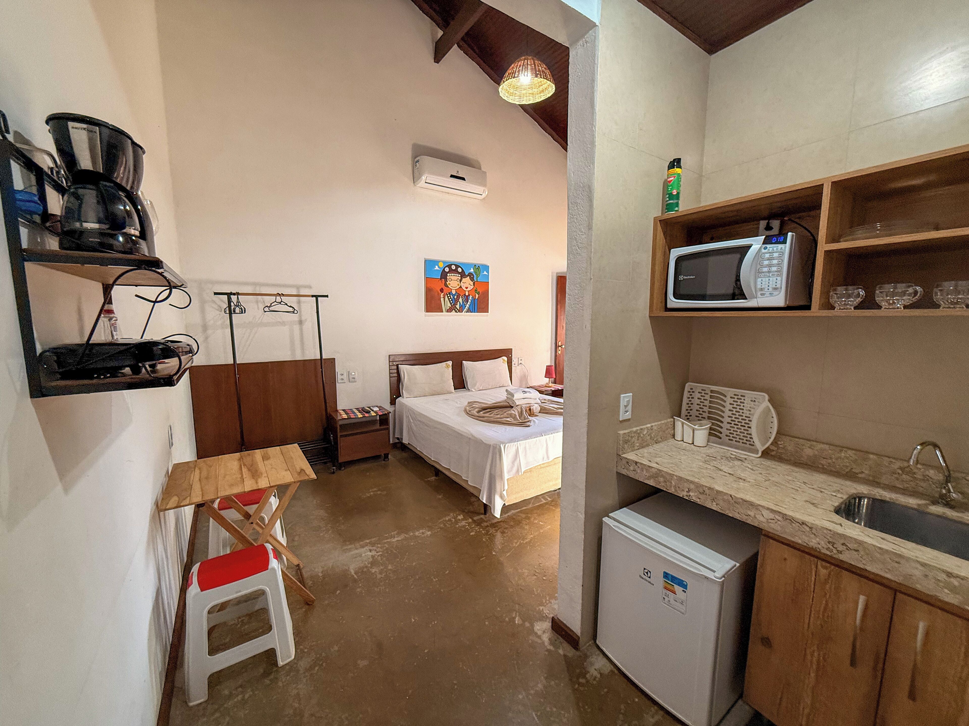 Een compacte hotelkamer met een bed, een kleine kitchenette, een koelkast, een magnetron en een plank met een koffiezetapparaat.