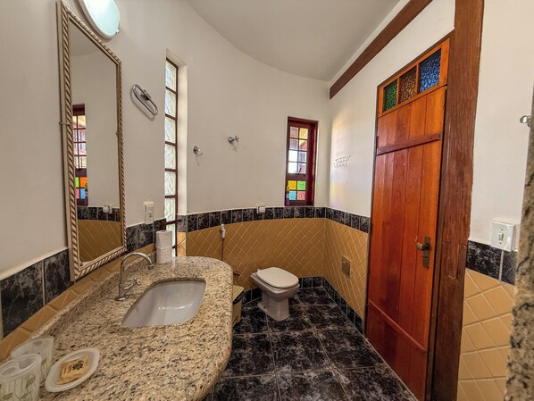 A bathroom with a granite sink, a toilet, a mirror, and a wooden door.