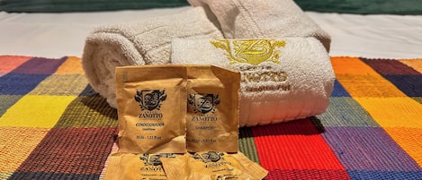 A bed with a colorful checkered bedspread, two towels, and two bags of toiletries.
