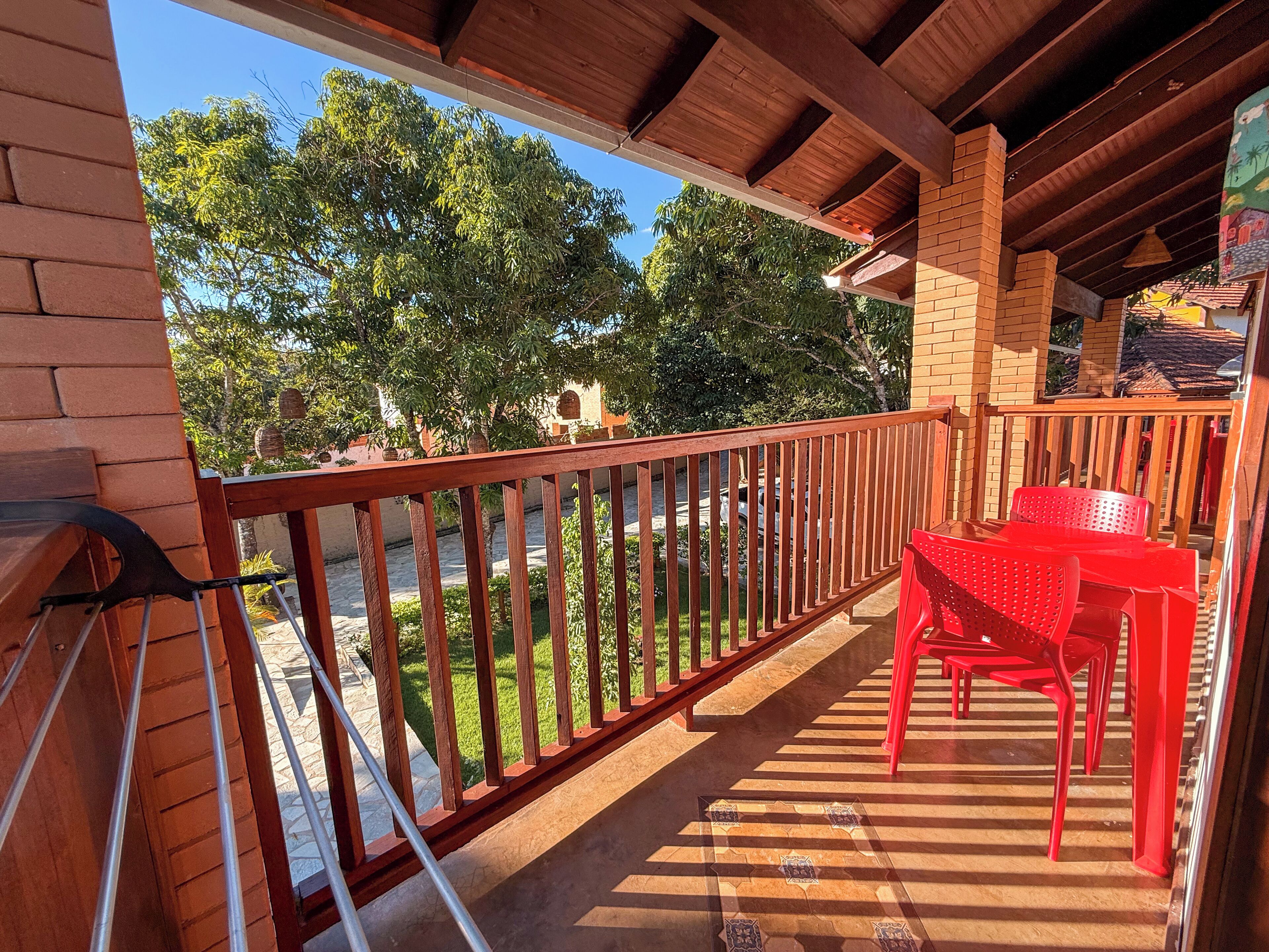 A balcony with a wooden railing, red plastic chairs, and a view of greenery and buildings in the background.