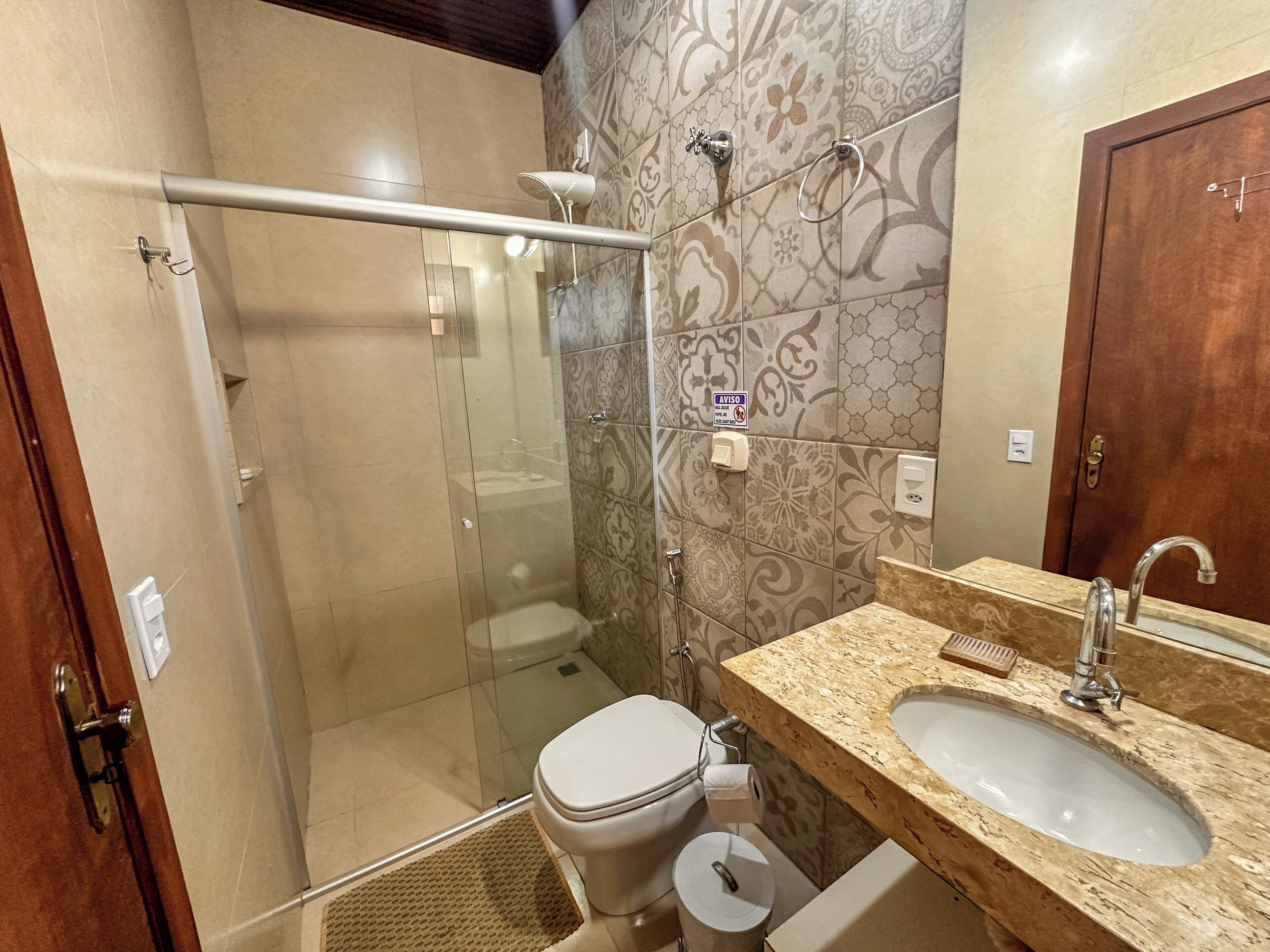 A bathroom with a glass-enclosed shower, a toilet, a sink, and a wooden door.