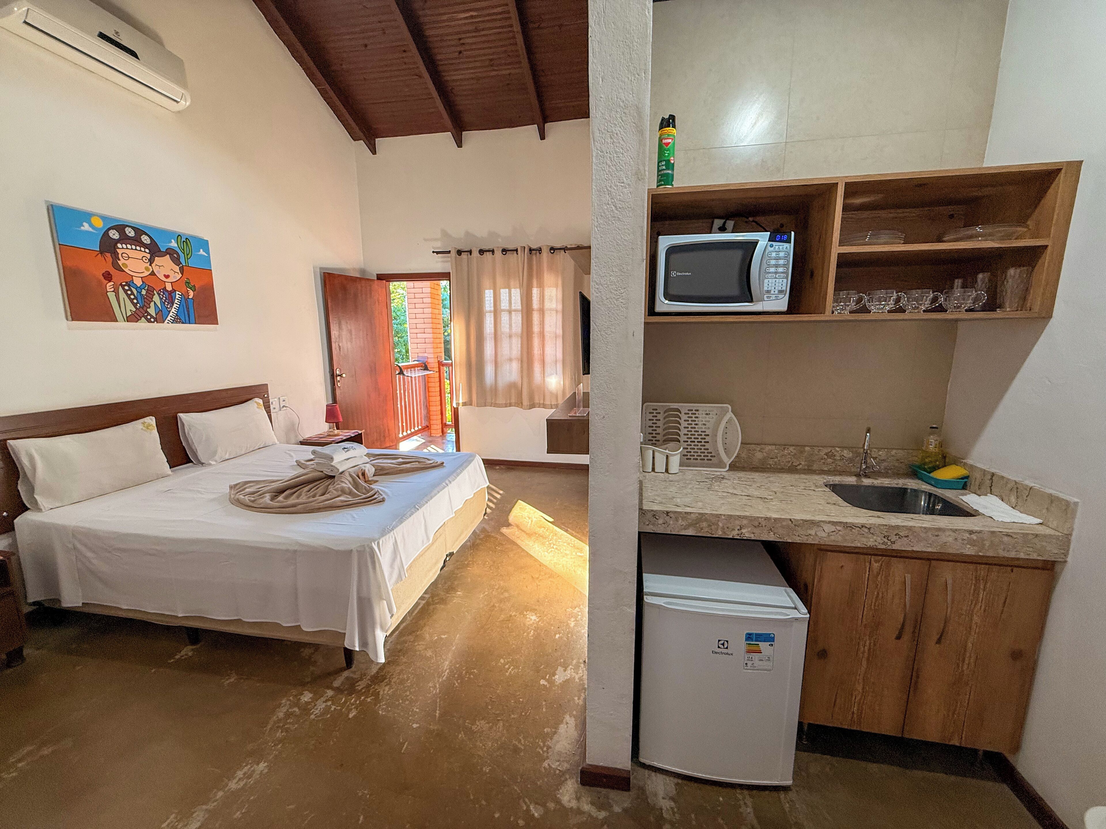 A hotel room with a bed, a small kitchenette, a television, and a refrigerator.
