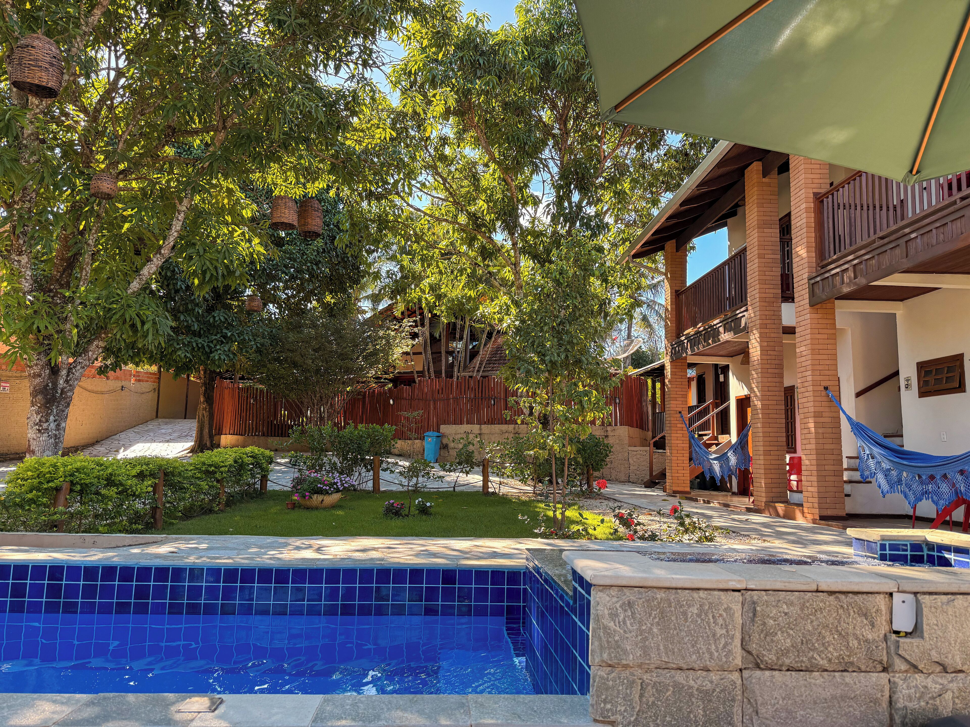 A pool area with a blue tiled edge, surrounded by a wooden fence, trees, and a building with balconies.