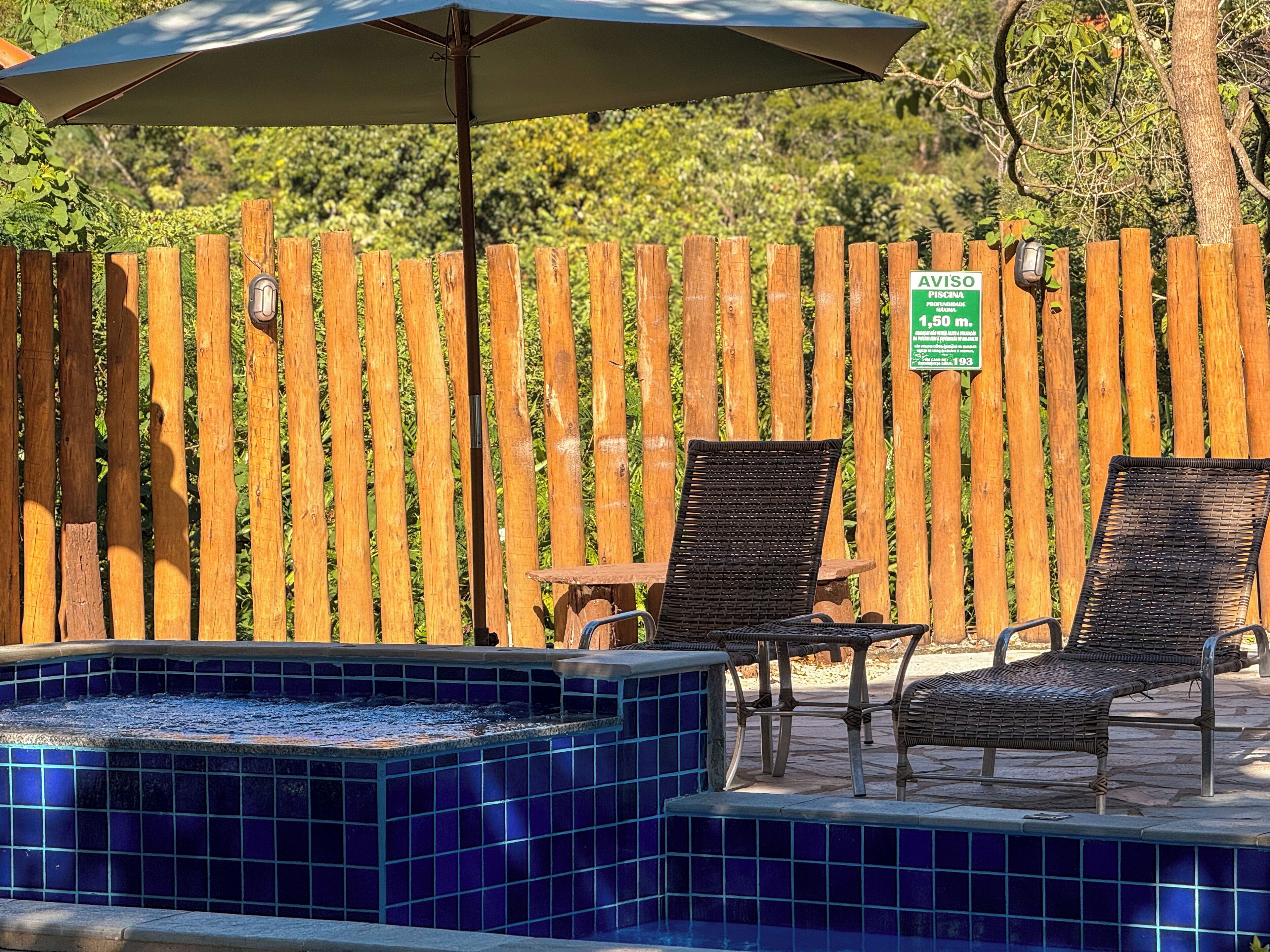 A small outdoor pool area with blue-tiled steps leading into the pool, two wicker chairs, and a wooden fence in the background.