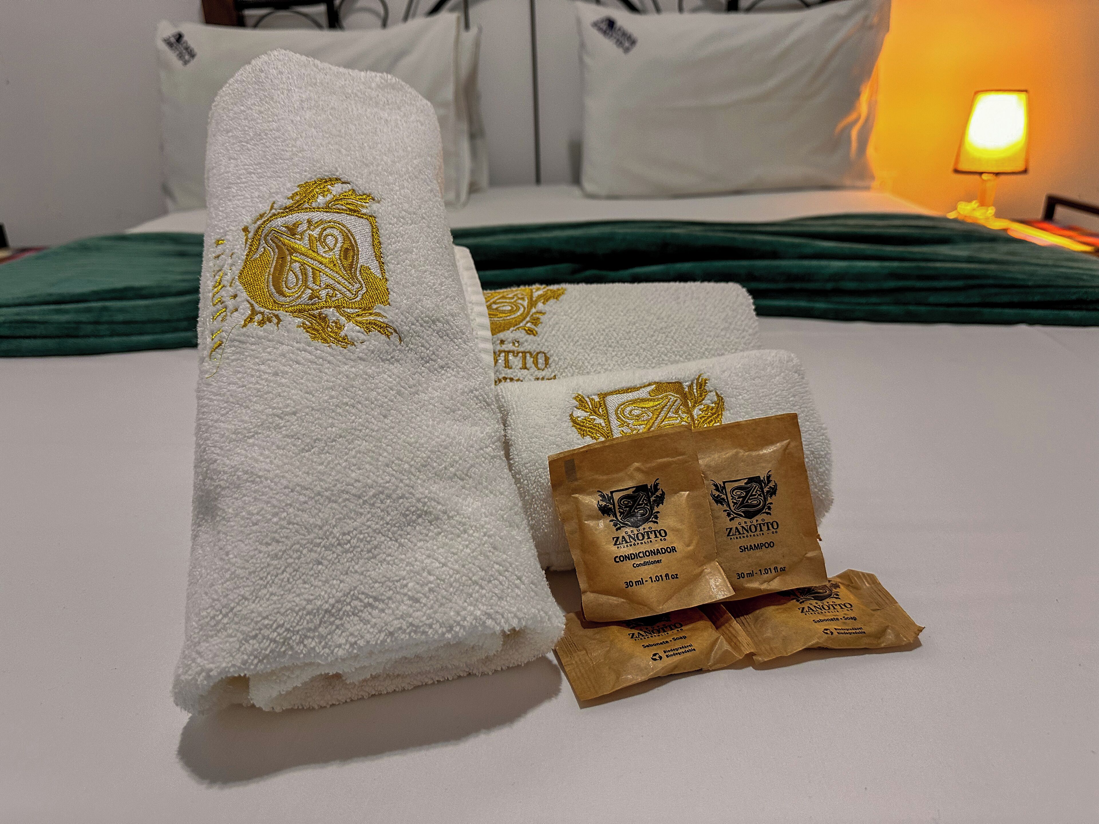Een net opgemaakt bed met witte handdoeken en twee flesjes shampoo.