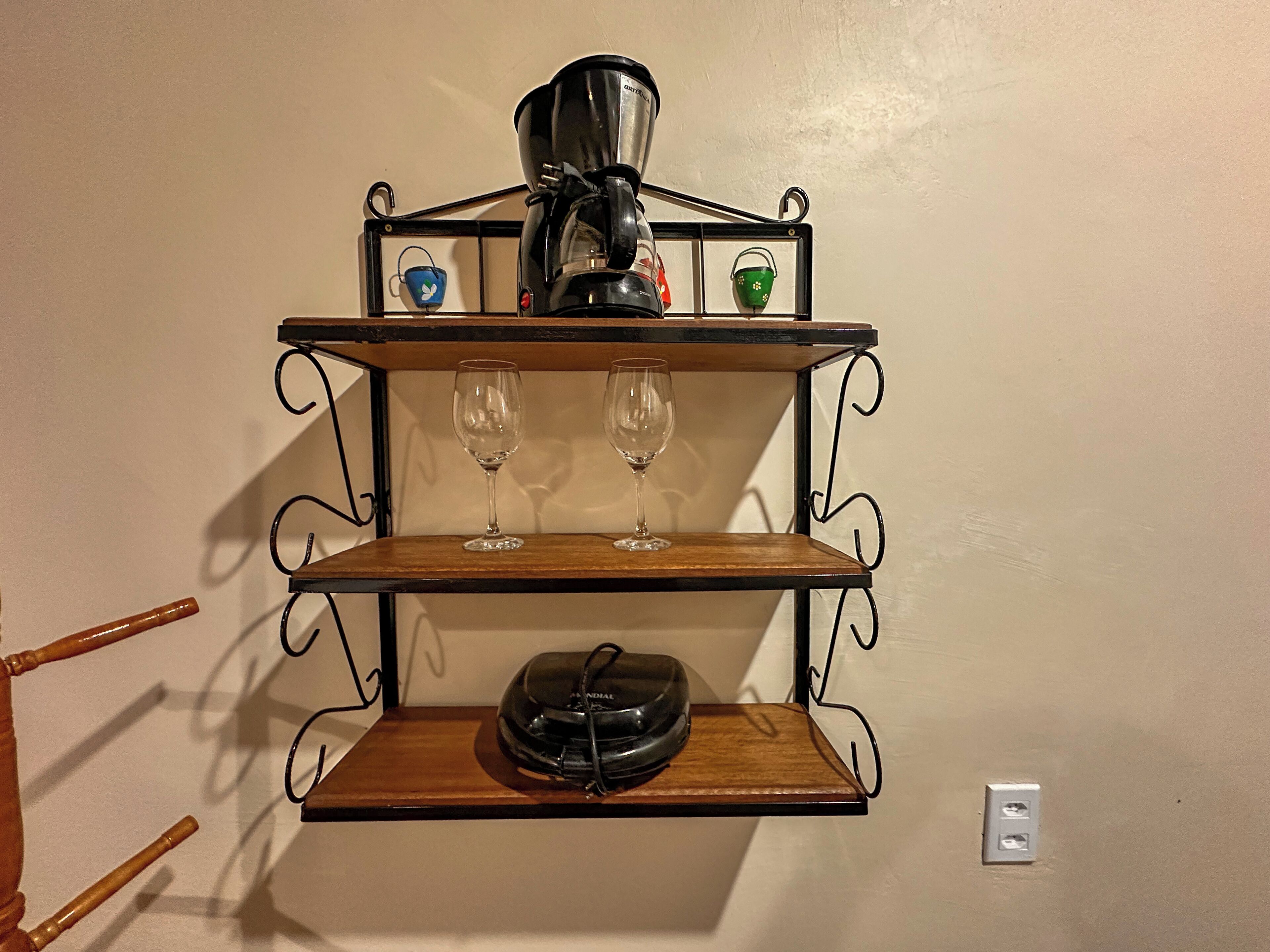 A wall-mounted shelf with a coffee maker, two wine glasses, and a bowl.