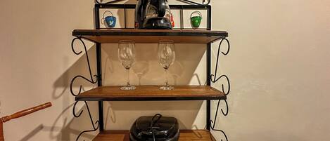 A wall-mounted shelf with a coffee maker, two wine glasses, and a bowl.