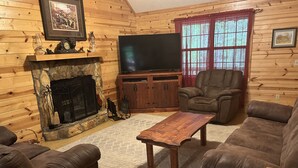A cozy living room with a stone fireplace, leather sofas, a wooden coffee table, and a television on a wooden cabinet. - Bear-A-Dise- A beautiful mountain cabin-sleeps 12, hot tub, game room & firepit. (Blairsville)