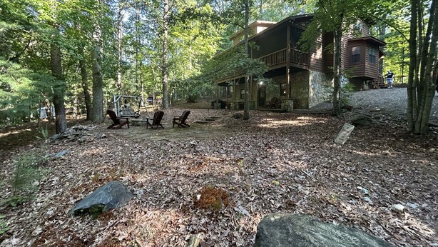 A cabin with a stone exterior and a wooden deck, surrounded by trees and a leaf-covered ground. - Bear-A-Dise- A beautiful mountain cabin-sleeps 12, hot tub, game room & firepit. (Blairsville)