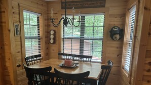 A wooden interior with a dining table, four chairs, a chandelier, and a clock on the wall. - Bear-A-Dise- A beautiful mountain cabin-sleeps 12, hot tub, game room & firepit. (Blairsville)