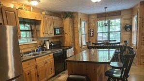 A wooden cabin-style kitchen with a refrigerator, stove, microwave, and sink. - Bear-A-Dise- A beautiful mountain cabin-sleeps 12, hot tub, game room & firepit. (Blairsville)