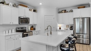 Een moderne keuken met witte kasten, roestvrijstalen apparatuur en een centraal eiland met een spoelbak en krukken.
