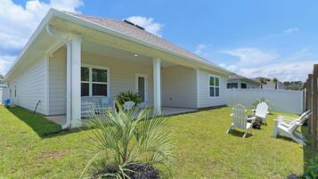 A single-story house with a covered porch, a small garden with a palm plant, and outdoor seating.
