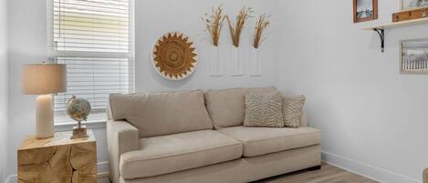 A neutral-toned living room with a beige sofa, a wooden side table, a globe, and a lamp.