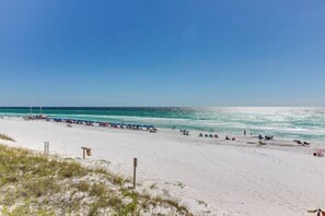 A beach with white sand and clear blue water. There are people and umbrellas along the shore.