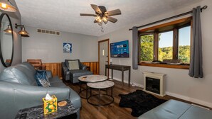 A living room with a sofa, two round tables, a ceiling fan, a fireplace, and a TV on a stand. - 4BR, 3.5 BA House, great sunset view, close to town. (Nashville)