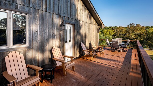 A wooden deck with Adirondack chairs and a table, overlooking a forested area. - 4BR, 3.5 BA House, great sunset view, close to town. (Nashville)