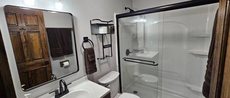 A modern bathroom with a wooden vanity, a toilet, a glass-enclosed shower, and a mirror with lights above the sink.