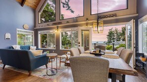 A spacious living room with a high ceiling, large windows, and a cozy seating area. - Polnell Point Lookout by Avantstay Water Views, Hot Tub, Large Patio (Oak Harbor)