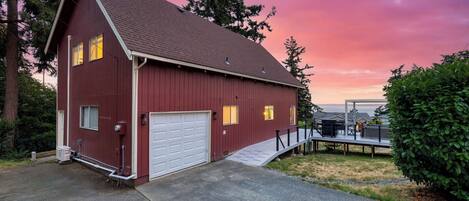 A red barn-style building with a garage, a deck, and a view of the ocean.