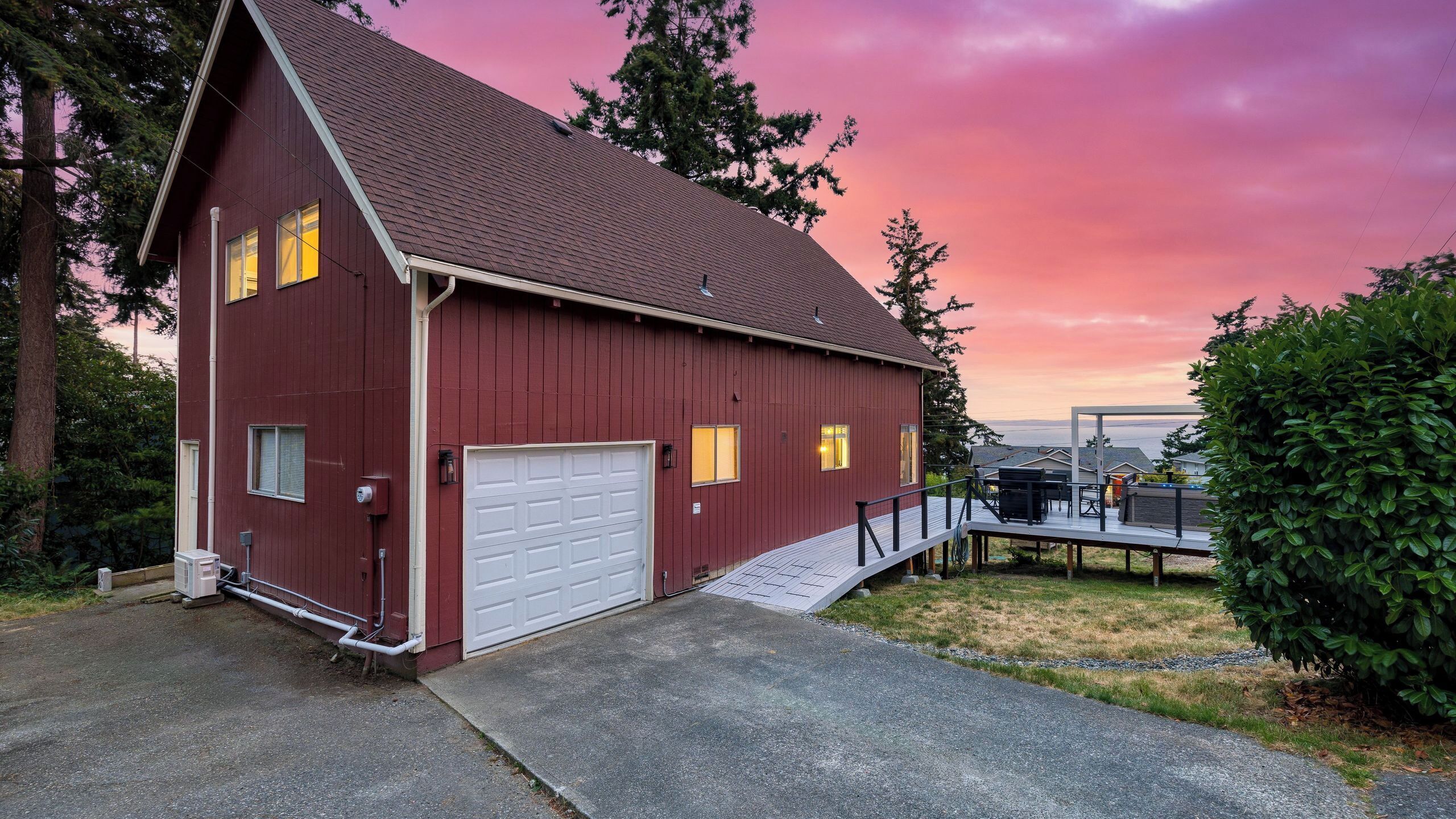 A red barn-style building with a garage, a deck, and a view of the ocean. - Polnell Point Lookout by Avantstay Water Views, Hot Tub, Large Patio (Oak Harbor)