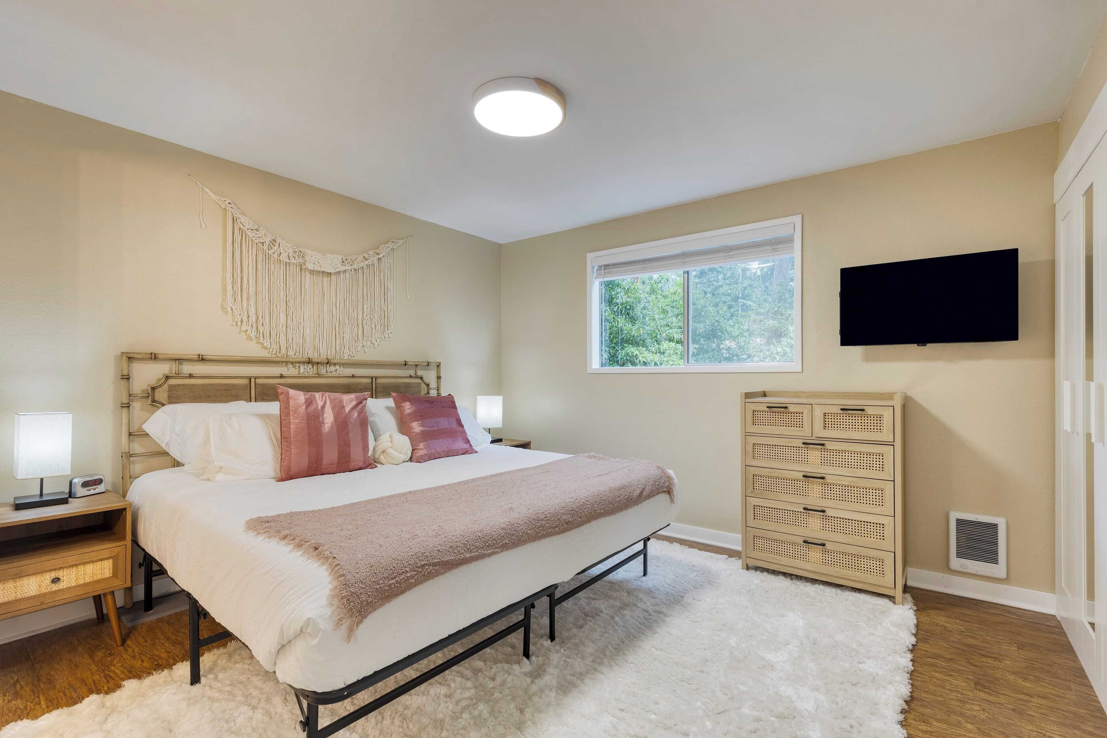 A bedroom with a bed, bedside tables, a dresser, a television, and a window.