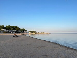 A beach with a pier extending into calm waters, surrounded by residential buildings and greenery. - 2-bedroom 2 bathroom bungalow with AC, WiFi in lovely Crystal Beach Niagara (Fort Erie)