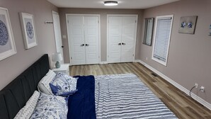 Un dormitorio con cama, una mesita de noche con lámpara, una ventana con persianas y una puerta.
