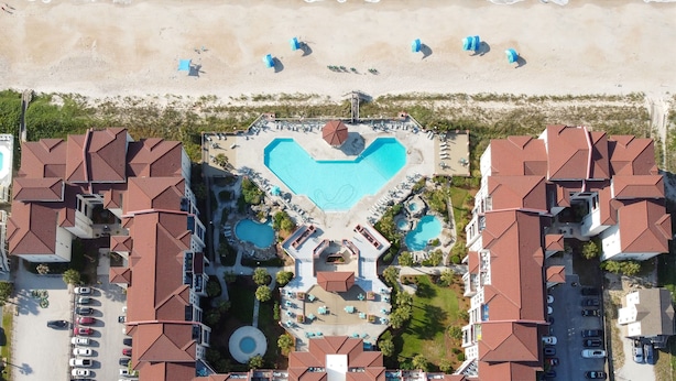 Une vue aérienne d’un complexe hôtelier avec une piscine centrale en forme de cœur, entourée de plusieurs petites piscines et d’une fontaine circulaire.