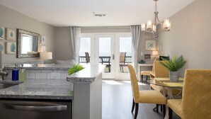 Une cuisine moderne avec un îlot central, un coin repas avec des chaises jaunes et une vue sur l’extérieur grâce à une porte vitrée.