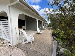 A covered outdoor seating area with white chairs and a table, surrounded by greenery and a stone pathway. - Apartment on gated resort, minutes from beautiful beaches (Sint Michiel)