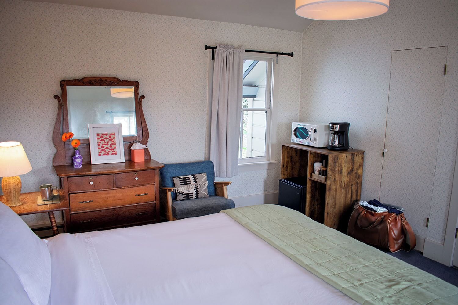 Un dormitorio con cama, cómoda, silla y un mueble de madera que incluye microondas y cafetera.