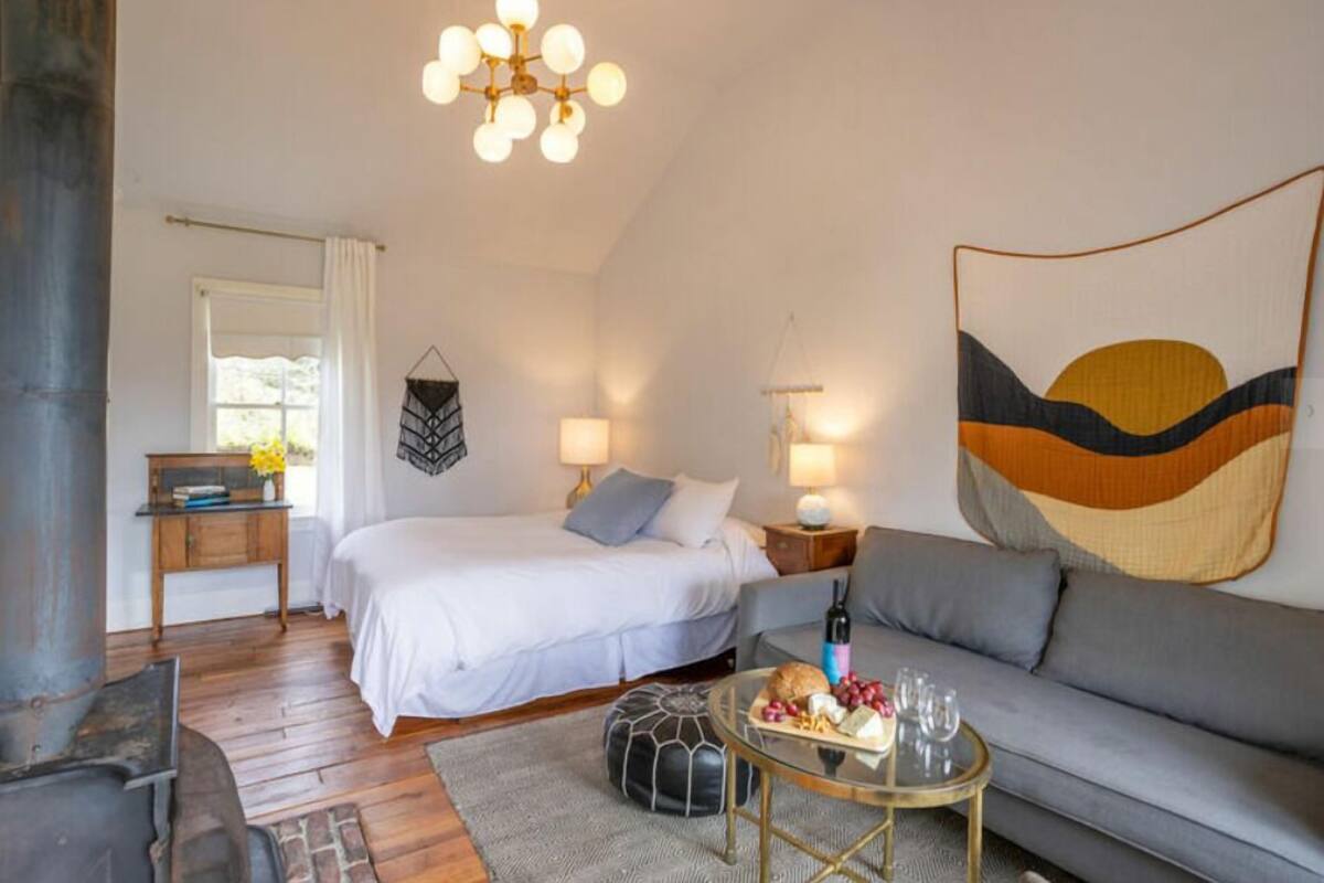 Un dormitorio acogedor con cama, mesitas de noche, un sofá, una mesa de centro de vidrio y una lámpara colgante.