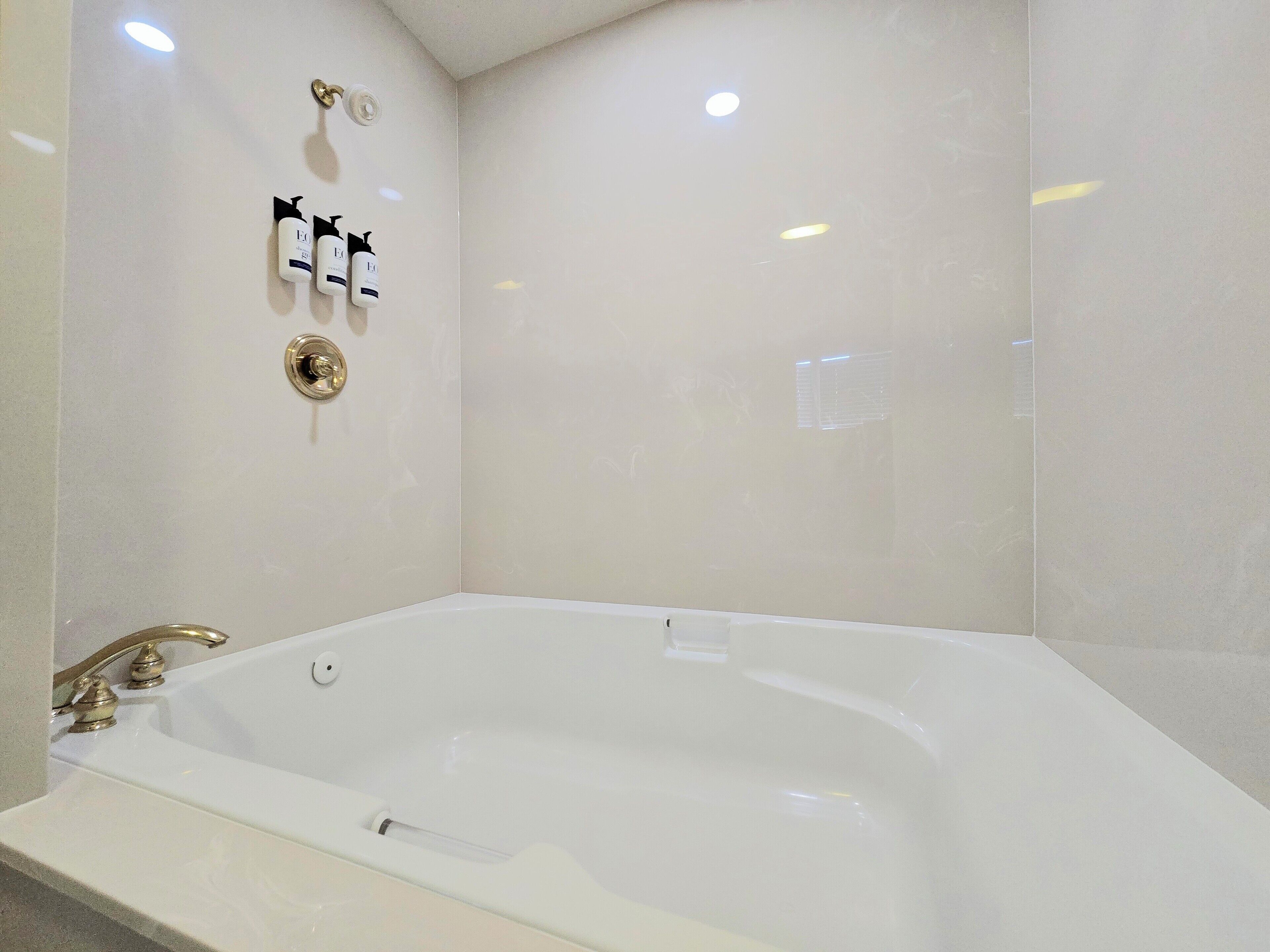 A modern bathroom with a large bathtub, a gold faucet, and two bottles of shampoo on the wall.