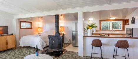 A cozy room with a bed, a small table, a bar area with stools, and a wood-burning stove.