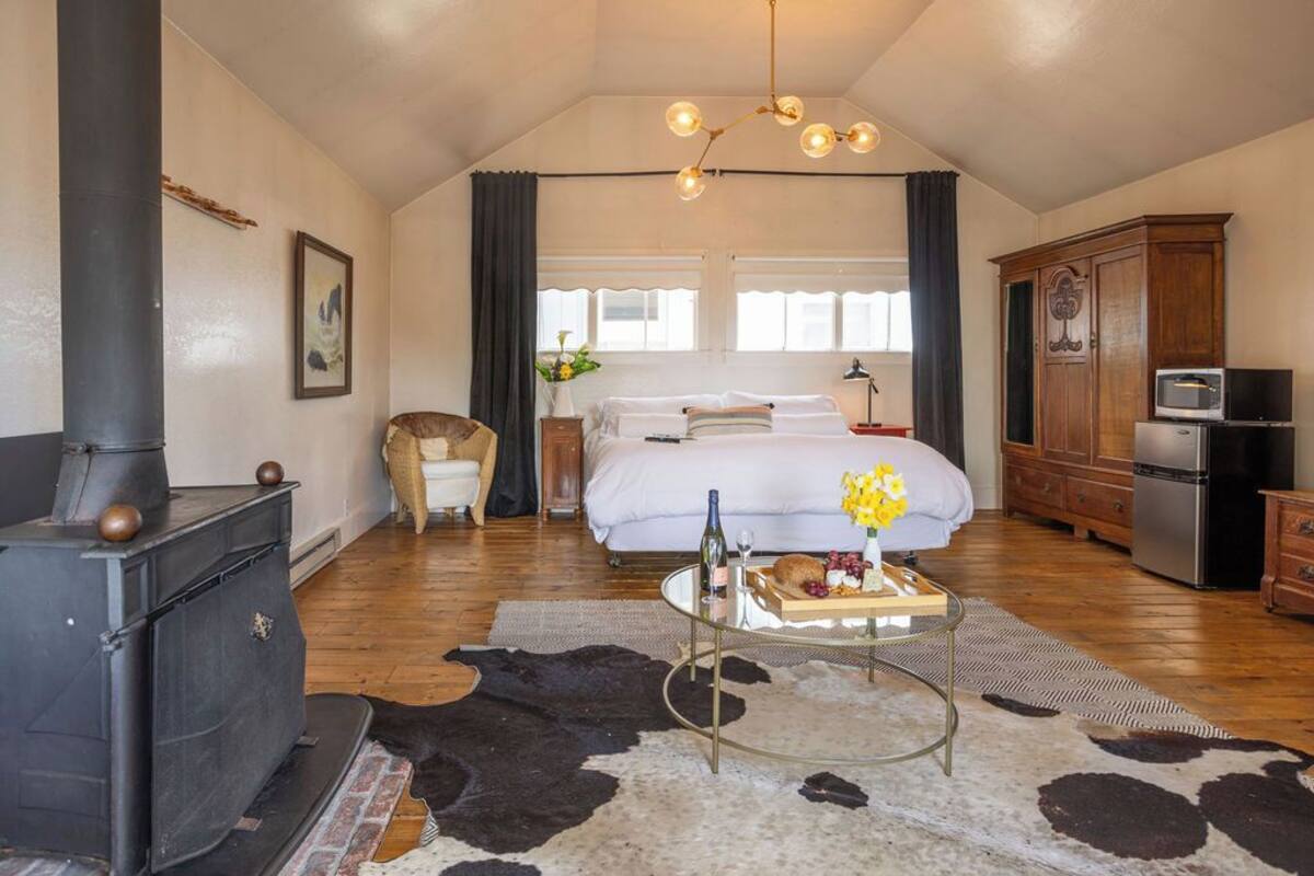 Un dormitorio acogedor con cama, cómoda de madera, estufa y alfombra de cuero de vaca.