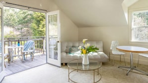 A cozy room with a sofa, a coffee table, and a dining table. There is a sliding glass door leading to an outdoor deck.