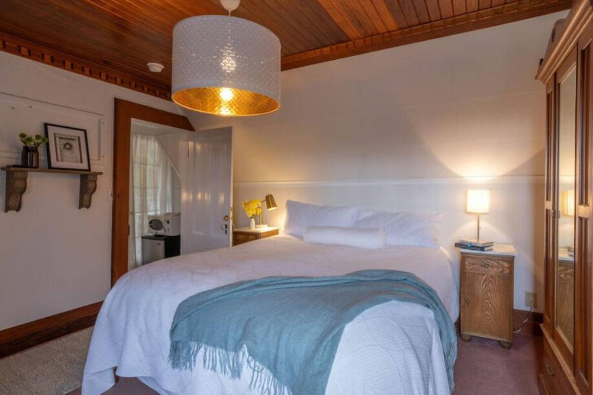 Un dormitorio con una cama grande, cabecera de madera, mesita de noche con lámpara y un armario.