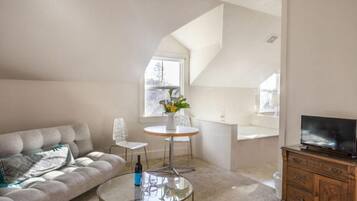 A modern living room with a sofa, a glass coffee table, a TV, and a dining area with a table and chairs.
