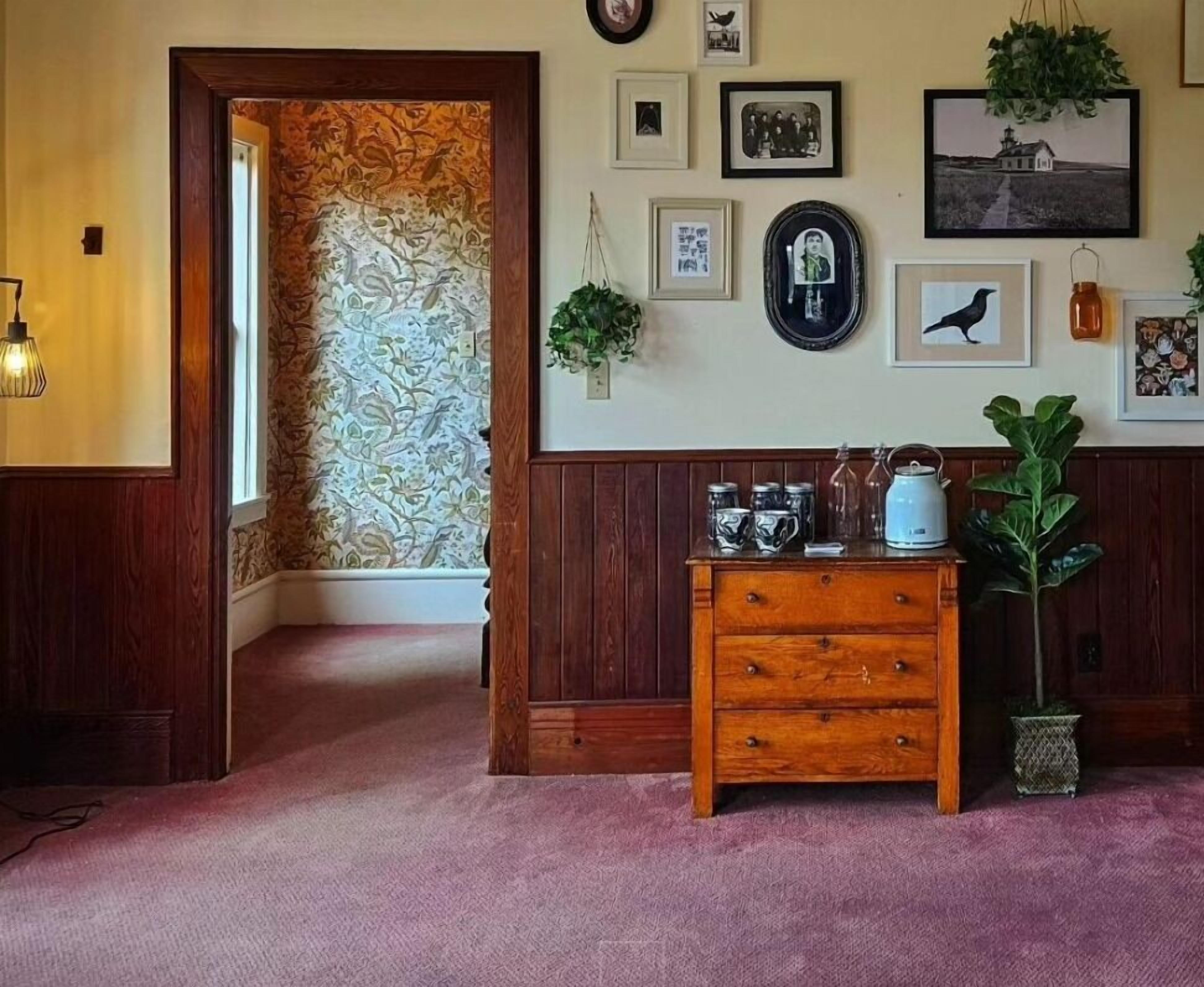A hallway with a wooden dresser, a potted plant, and framed pictures on the wall.