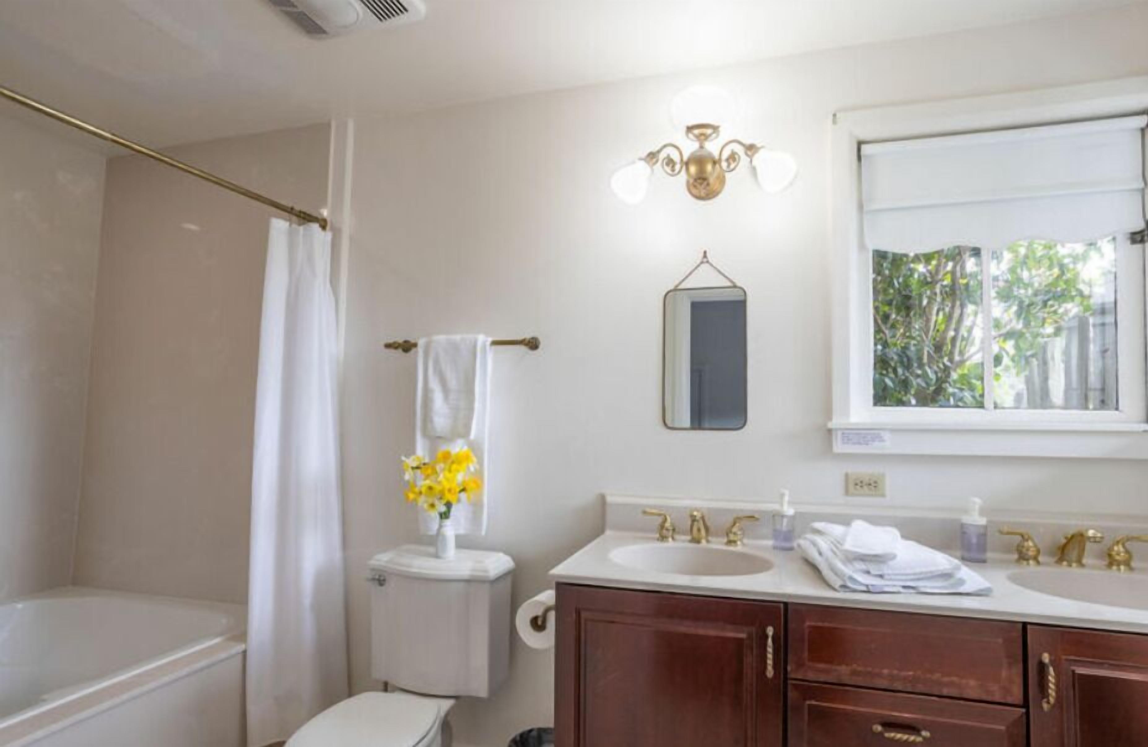A bathroom with a bathtub, toilet, sink, vanity, and a mirror.