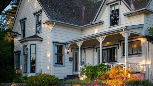 A two-story house with a porch, multiple windows, and a stone foundation.