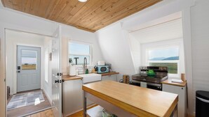 Une cuisine avec une table en bois, des placards blancs, une cuisinière et une fenêtre donnant sur les montagnes.