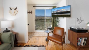 Un salon comprenant un canapé, un fauteuil, un téléviseur, un meuble en bois et une vue sur l’extérieur, accessible par une porte coulissante.