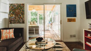 Una sala de estar con sofá, una mesa de centro de vidrio y vistas a un patio exterior a través de una puerta corrediza de vidrio.